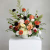 Mixed bouquet in a white bowl vase with peach, white, orange, and burgundy flowers