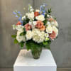 Wedding bouquet in a glass vase with white, peach, and blue flowers