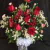 Red roses and red alstroemeria in a clear vase with white ribbon