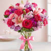 Pink roses and lilies arranged in a glass vase with a pink ribbon