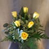 Yellow roses arranged in a glass vase with mixed greenery