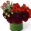 Red and burgundy flowers arranged in a green glass vase