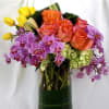 Bouquet of orange roses, purple orchids, and yellow tulips in a glass vase