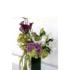 Purple roses, white lilies, and green orchids in a tall glass vase