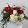 Red roses and white hydrangeas in a white vase with pine and berry accents