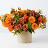 Orange and peach floral arrangement in a beige vase