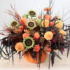 Orange and black floral arrangement in a pumpkin container with sunflowers and mums