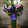 Mixed bouquet of lilies, roses, and hydrangeas in a tall green vase