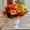Orange and pink roses in a white vase with dried accents