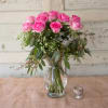 Pink roses arranged in a clear glass vase with greenery