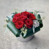 Red roses arranged in a low box with a jeweled brooch accent