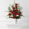 Multiple red roses with white filler and palm-like greenery, arranged upright in