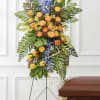 Tall, structured standing easel with orange roses, yellow pom-poms, blue delphinium and