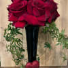Red roses in a tall black vase with trailing greenery and a glittery heart
