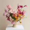 Pink and peach mixed flower arrangement in a ribbed cream vase