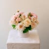 Low arrangement of blush roses, white hydrangeas, and soft pink mums in a white ribbed ceramic vase