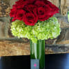 Red roses above a green hydrangea cluster in a tall glass vase