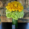 Yellow roses arranged with pale green hydrangeas in a tall green vase