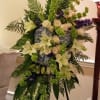 Tall standing spray of white lilies, roses, blue hydrangeas, and green bells of Ireland on an easel