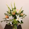 Tall arrangement of white lilies and peach roses with green hydrangea in a clear glass vase