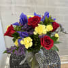 Bouquet of red roses, yellow carnations, and purple flowers in a glass vase