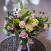 Pink roses and lilies arranged in a vase with a pink ribbon