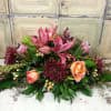 Low floral arrangement with pink lilies, peach roses, and burgundy blooms