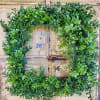 Square greenery wreath with dense green leaves on a rustic background