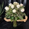 White roses arranged in a glass vase with greenery and small filler flowers
