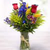 Mixed bouquet of roses, lilies, and blue flowers in a glass vase