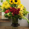 Bouquet of sunflowers, red roses, and yellow orchids in a tall glass vase