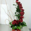Tall arrangement of red roses in a black box with curly branches