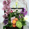 Mixed floral arrangement in a dark rectangular container with orchids and calla lilies