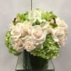 White roses and calla lilies arranged with green hydrangeas in a glass vase