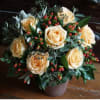 Cream roses arranged in a brown pot with red berries and greenery.