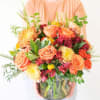 Mixed bouquet of peach roses and orange blooms in a glass vase