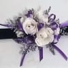 White floral wrist corsage with purple ribbon on a black band