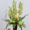 Tall green floral arrangement in a black vase with a pink candle beside it