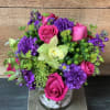 Pink roses and purple flowers arranged in a rustic white vase