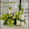 Green and white floral centerpiece with hydrangeas, roses, and tall blooms on a table