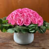 Low dome of bright pink roses with a ring of greenery in a white ceramic vase