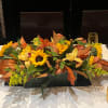 Low floral centerpiece with sunflowers and autumn-colored blooms on a table