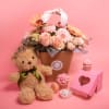 Flower basket with roses and gerberas, plus a teddy bear and cupcakes on a pink background