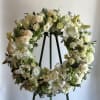 A white wreath filled with Star gazer lilies, lisianthus, roses, and bells