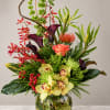 Tropical floral arrangement in a glass vase with orchids, calla lilies, and red accents