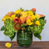 Yellow and peach floral arrangement in a glass vase with hydrangeas and roses