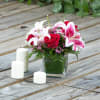 Red roses and pink lilies in a square glass vase with white candles