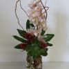 Pink orchids arranged in a glass vase with succulents and red accents