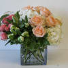 Bouquet of peach and pink roses with white hydrangeas in a square glass vase