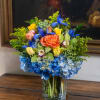 Arranged with Summer flowers including orange roses, yellow spray roses, blue hydrangeas